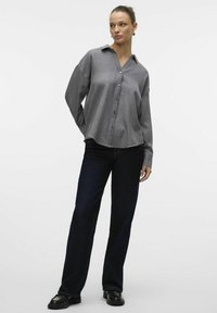 Gray button-up shirt with a structured collar and long sleeves; paired with dark blue straight-leg jeans; smooth fabric texture.
