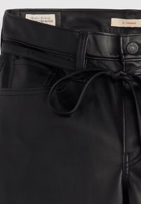 Czarne spodnie z ekoskóry o prostym kroju, z przewiązką w talii, kieszeniami z przodu oraz widocznymi detalami w szwie.