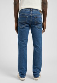 Pantalones vaqueros de mezclilla azul oscuro con un corte recto, que cuentan con bolsillos traseros y costuras amarillas. Terminados con una clásica etiqueta de logotipo en la cinturilla.