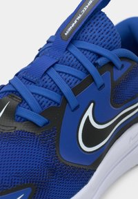 Μπλε αθλητικό παπούτσι με υφή από πλέγμα, μαύρες λεπτομέρειες και λευκό λογότυπο Swoosh. Διαθέτει φαρδιά κορδόνια και μορφοποιημένα στοιχεία για σταθερότητα.