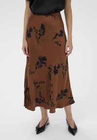 Jupe midi en tissu léger à motif floral marron, avec des imprimés de fleurs noirs. Assortie avec des chaussures noires à bouts pointus.