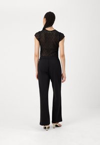 Μαύρη δαντελένι�α μπλούζα με κοντά μανίκια, συνδυασμένη με μαύρα παντελόνια σε φαρδιά γραμμή και ψηλοτάκουνες σάντες. Απλός, υφασματικός σχεδιασμός με ελαστική μέση.