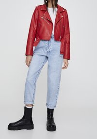 Röd läderjacka i kort bikerstil med silverfärgade dragkedjor, parat med ljusblå högmidjade jeans och svarta ankelskot med tjocka sulor.