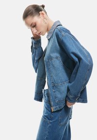 Jeansjacke mit strukturiertem Schnitt, ausgestattet mit einem gestreiften Kragen, vorderen Taschen und einem Reißverschluss. Farbe Blau und strukturierten Stoff.