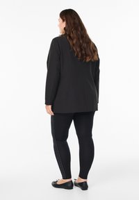Blazer negro de manga larga y corte recto, combinado con leggings negros que tienen acentos de tachuelas blancas a lo largo del costado. Bailarinas negras.