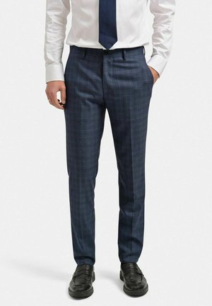 Marinblå rutiga kostymbyxor med skräddarsydd passform, som har en slät yta och sidofickor, ihop med svarta loafers och en vit skjorta.