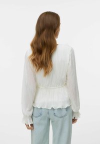 Hvit plissert topp med lange ermer og volangmanchetter, innsnevret i midjen, kombinert med lyseblå vide bukser.