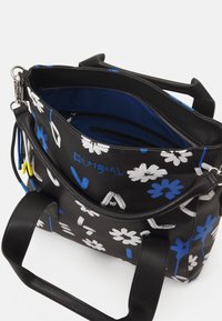 Schwarze Handtasche mit weißen und blauen Blumenmustern, kurzen schwarzen Griffen und einem blauen Innenraum mit Reißverschluss- und Einschubtaschen.