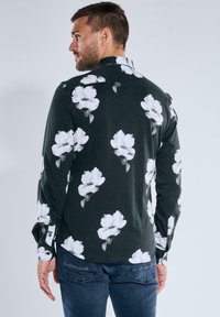 Langärmliges Hemd aus schwarzem Stoff mit einem weißen Blumenmuster. Regelkragen, geknöpfte Manschetten und ein abgerundeter Saum.