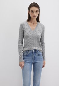 Grauer kabelgestrickter Pullover mit V-Ausschnitt, langen Ärmeln und geripptem Saum. Getragen mit hellblauen Jeans, schmeichelnder Textur und taillierter Passform.
