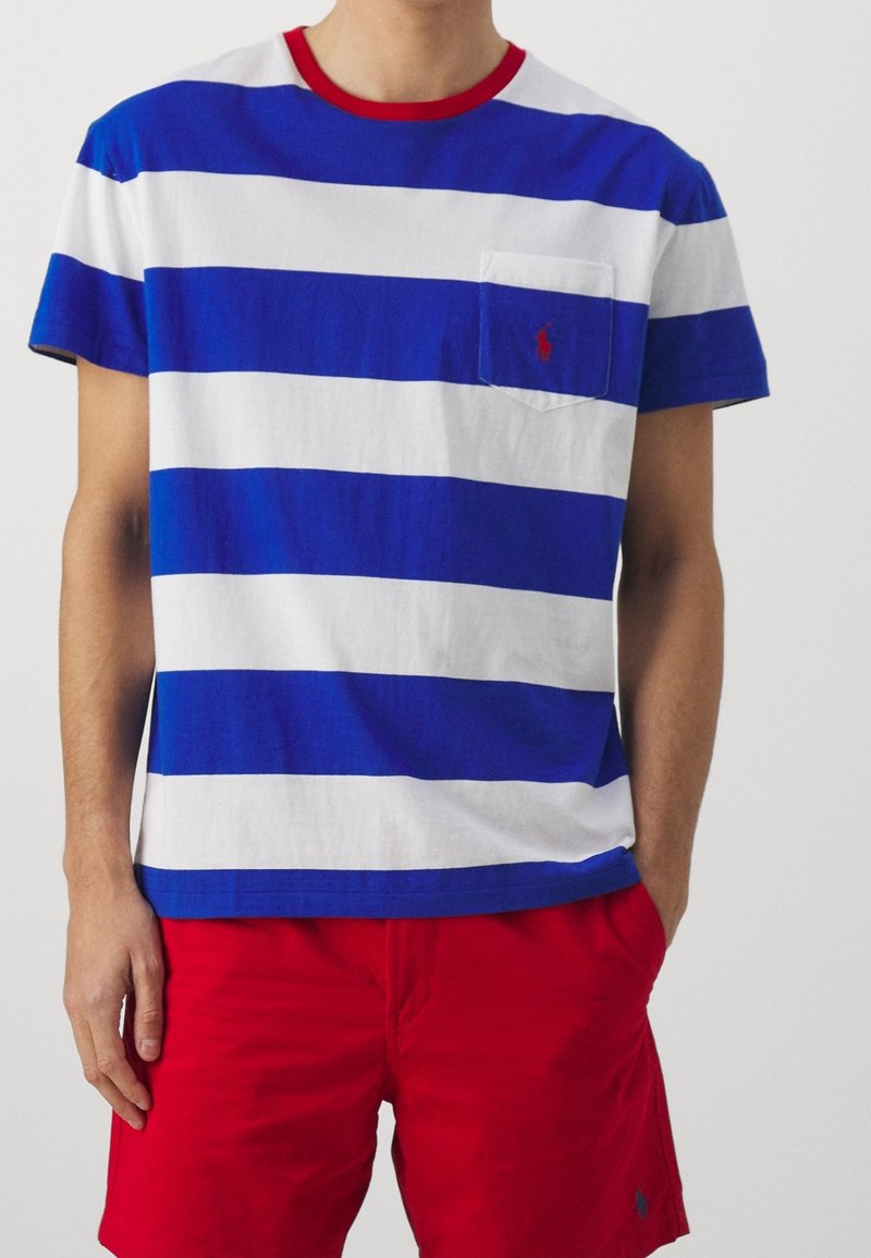 Bomullströja med blå och vita horisontella ränder, röd ribbad krage, ficka på vänster bröst, matchad med röda shorts.