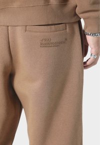 Ruske bomullsweatpants med en teksturert finish. Har en baklomme og preget logo "IRASUTO STUDIOS" nær midjen.