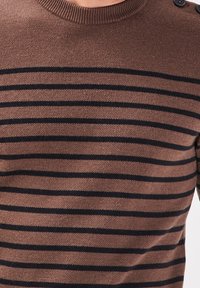 Brauner Strickpullover mit horizontalen schwarzen Streifen, rundem Halsausschnitt und Knöpfen an den Schultern. Das Material wirkt weich mit einer strukturierten Oberfläche.