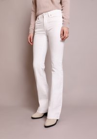 Vaqueros acampanados blancos de denim, con una cintura alta, cinco bolsillos y un acabado sutilmente texturizado. Combinados con botas de tobillo de color claro.