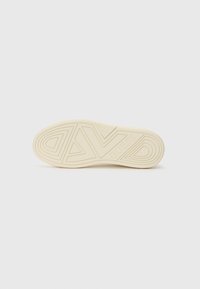 Hvit gummisåle på sneakers med et teksturert mønster og logo-detalj. Formen er avrundet med en flat bunn for stabilitet.