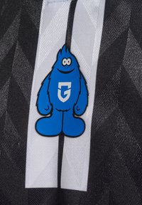 Blauer Cartoon-Charakter mit runden Augen und bartartiger Form steht auf schwarz-weiß vertikal gestreiftem Stoff mit geometrischen Mustern.