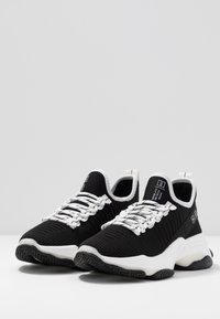 Baskets noires en maille avec accents blancs. Elles présentent une tige texturée, une semelle épaisse blanche et une semelle extérieure en caoutchouc à motifs. Les lacets sont plats et tissés.