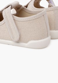 Beige plátěné boty se suchým zipem, texturovaný svršek a bílá gumová podrážka. Zaoblený design s nízkým profilem a jednoduchými švy.