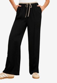 Pantalons noirs à jambes larges avec une taille à cordon, poches avant et une texture de tissu douce. Accentué par une ceinture beige.