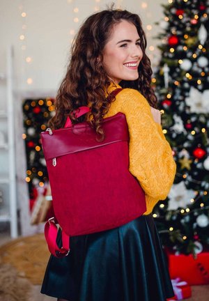 Dunkelroter Rucksack aus strukturiertem Stoff mit Lederakzenten, rechteckige Form, verstellbare rosa Träger, Reißverschlüsse, getragen mit einem gelben Pullover.