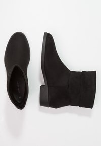 Bottines noires en daim avec un bout rond, un petit talon carré et un design flou. L'intérieur présente une semelle intérieure texturée.