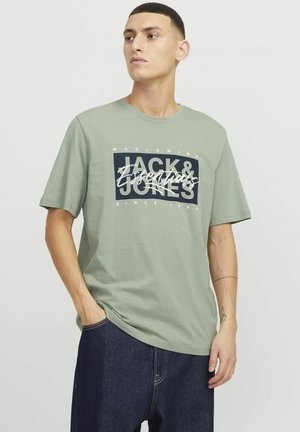 Lichtgroene katoenen T-shirt met een gedurfde grafische afbeelding in zwart en wit, met "JACK & JONES" en "Essentials" prominently weergegeven.