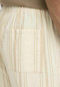 Pantalones ligeros a rayas con una textura suave, que presentan una combinación de colores beige y crema, además de un bolsillo externo en la parte posterior.