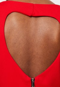 Robe rouge avec une découpe en forme de cœur dans le dos et un détail de fermeture éclair au bas du dos, présentée avec une texture de tissu lisse et des lignes épurées.