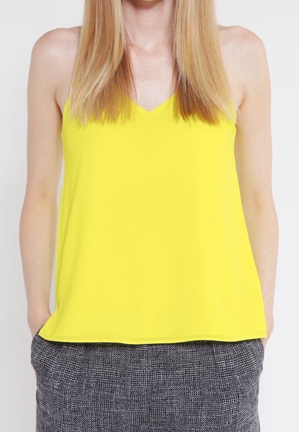 Haut jaune sans manches avec un col en V. Confectionné dans un tissu lisse, avec une coupe décontractée et sans ornements. Associé à un bas gris texturé.
