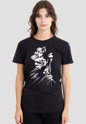Young woman with long hair wearing a black t-shirt featuring a white graphic of a person holding a sword and another figure in motion.