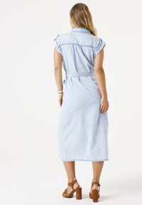 Hemdrobe aus hellblauem Denim mit kurzen, umgeschlagenen Ärmeln, einem taillierten Gürtel und Midi-Länge. Braune Riemchen-Absätze runden den Look ab.