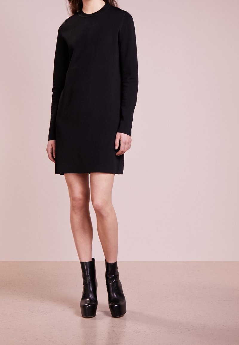 Abito in maglia nero a maniche lunghe con scollo rotondo. Presenta una silhouette dritta e sottili spacchi laterali. Abbinato a stivaletti neri con tacco platform.