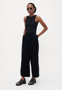 Svart, cropped tanktop, svarte bukser med vide ben og frontfolder, samt chunky svarte sko med metalliske detaljer. Tilbehøret inkluderer runde solbriller.