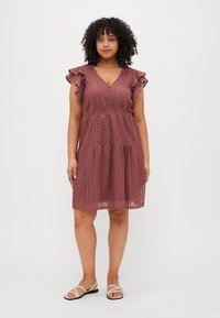 A knee-length, flared dress in dusty rose with lace detailing, short ruffled sleeves, and a gathered waist. Worn with flat sandals.