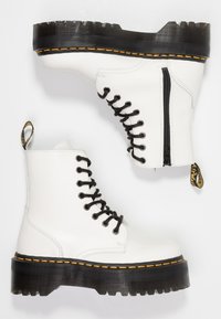 Botas de tobillo de cuero blanco con cordones negros, cremallera lateral y suela de plataforma negra acanalada con costuras amarillas. Incluye una lengüeta.