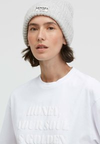 Gray knitted beanie with a logo patch, worn over white cotton T-shirt featuring textured text reading "HONEY, YOUR SOUL IS GOLDEN."