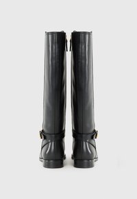 Rear view of tall, black leather boots with a side zipper and a decorative strap, set against a plain white background.