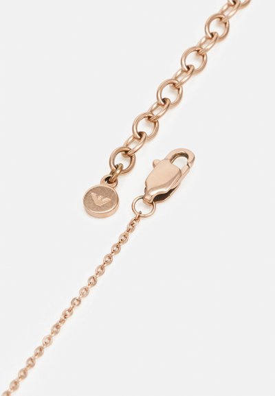 Kette aus roségoldfarbenem Metall mit runden Gliedern und einem Karabinerverschluss. An der Kette hängt ein kreisförmiges Etikett mit einem erhabenen Emblem.