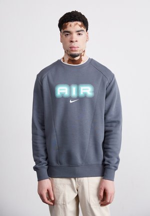Felpa grigia con scollo rotondo, caratterizzata da un testo blu "AIR" a strati e un piccolo logo Nike. Tessuto morbido con polsini e fondo a costine.