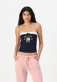 Navy strapless top with white detailing and graphic print stating "NEW YORK 28 CITY," paired with loose pink pants.