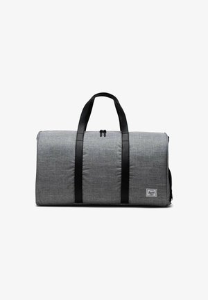 Sac de voyage gris avec poignées et accents en cuir noir. Présente un design rectangulaire robuste et une patch logo à l'avant. Fermeture éclair sur le dessus.