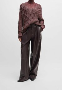 Pull en grosse maille bordeaux à col en V, associé à un pantalon large en cuir marron foncé. Tissu texturé et coupe décontractée.