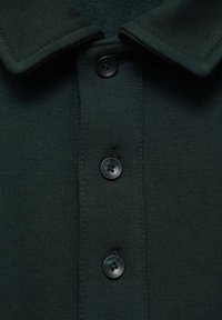 Dark green polo shirt featuring a button placket with three black buttons and a classic collar, made from ribbed fabric.