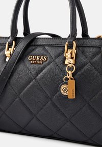 Sac à main en cuir noir avec motif matelassé, ferrures dorées, et étiquette charm avec logo. Poignées solides pour un transport facile.