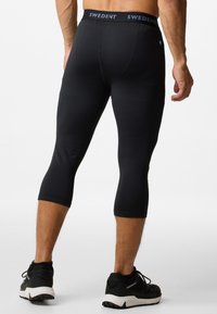 Black athletic leggings with a fitted design and knee-length cut. Features a branded waistband and smooth, elastic material.