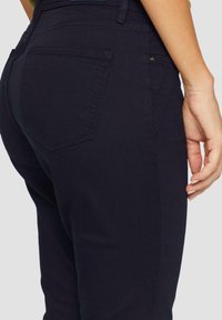 Jeans de un oscuro tono navy mostrados por la parte de atrás, con un diseño ajustado que incluye dos bolsillos traseros y costuras limpias. El material parece suave y elástico.