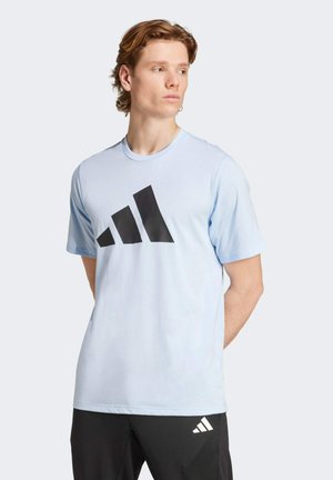Lyseblå bomulds T-shirt med rund hals og korte ærmer, med et stort sort tre-stribet logo over brystet og en glat tekstur.