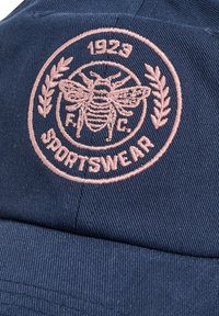Marineblauwe pet met roze geborduurd bijenlogo, lauriertakken, "1923", "F.C." en "SPORTSWEAR" tekst op het voorpaneel.