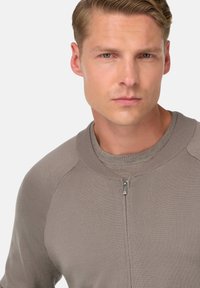 Suéter de punto gris con cuello con cremallera, textura acanalada y mangas raglán, que presenta un diseño suave y casual.
