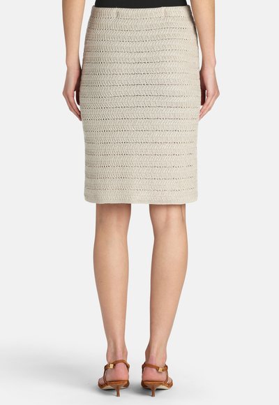 Femme portant une jupe crayon beige texturée jusqu'aux genoux et des sandales à talons marron, debout de dos sur un fond blanc.